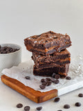 Stack of brownies on a wooden board with chocolate chips around.