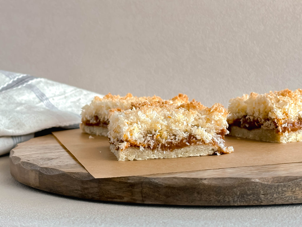 Two coconut dulce de leche dessert bars on a wooden board with a neutral background