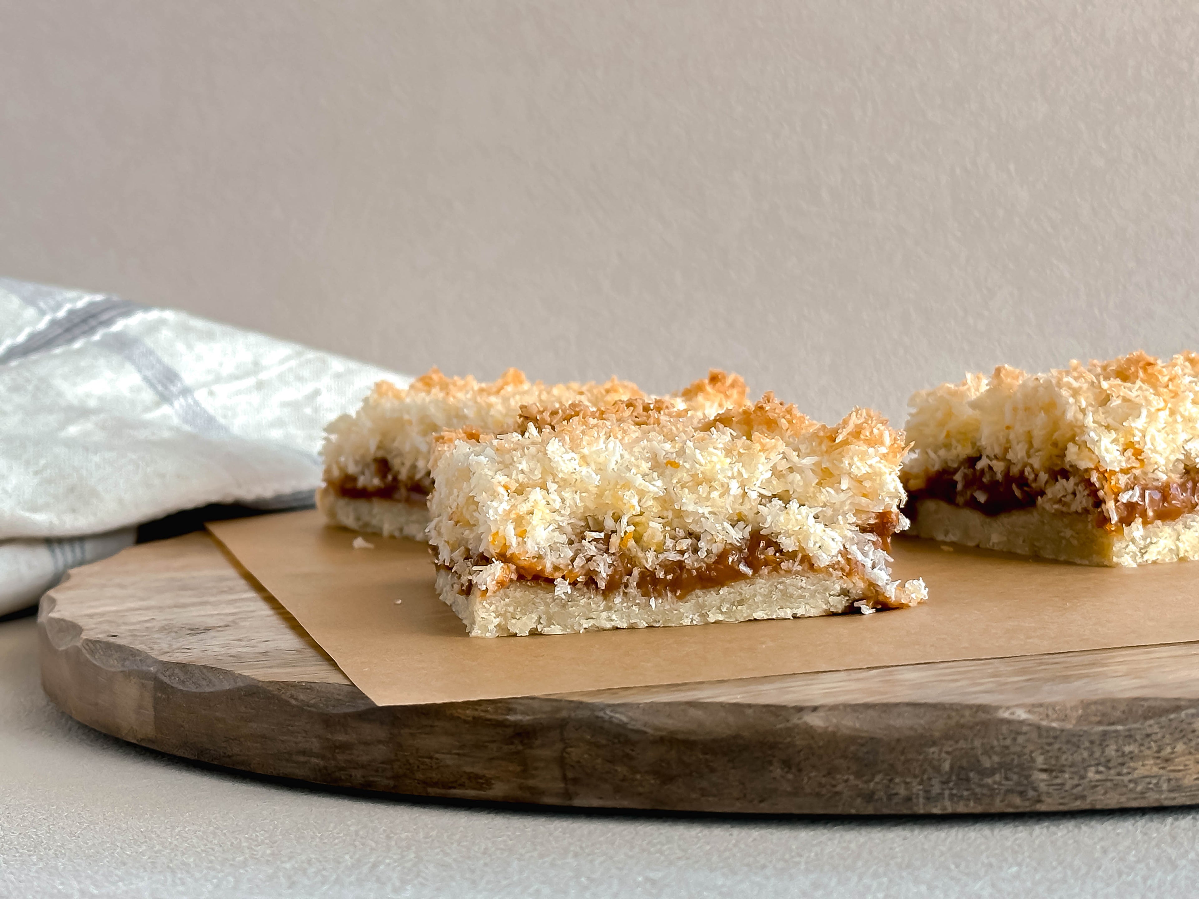 Two coconut dulce de leche dessert bars on a wooden board with a neutral background