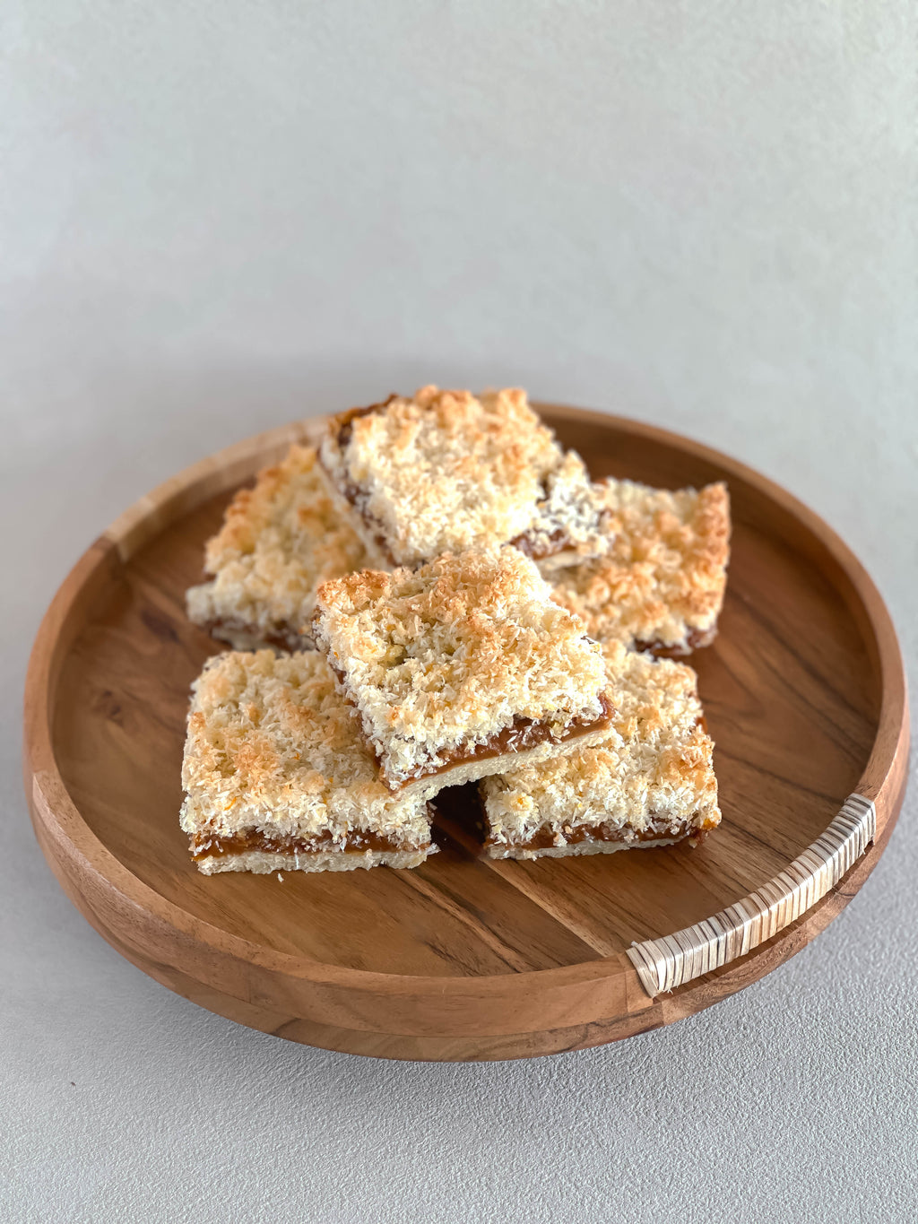 Three coconut dulce de leche dessert bars on a wooden plate with a light gray background.