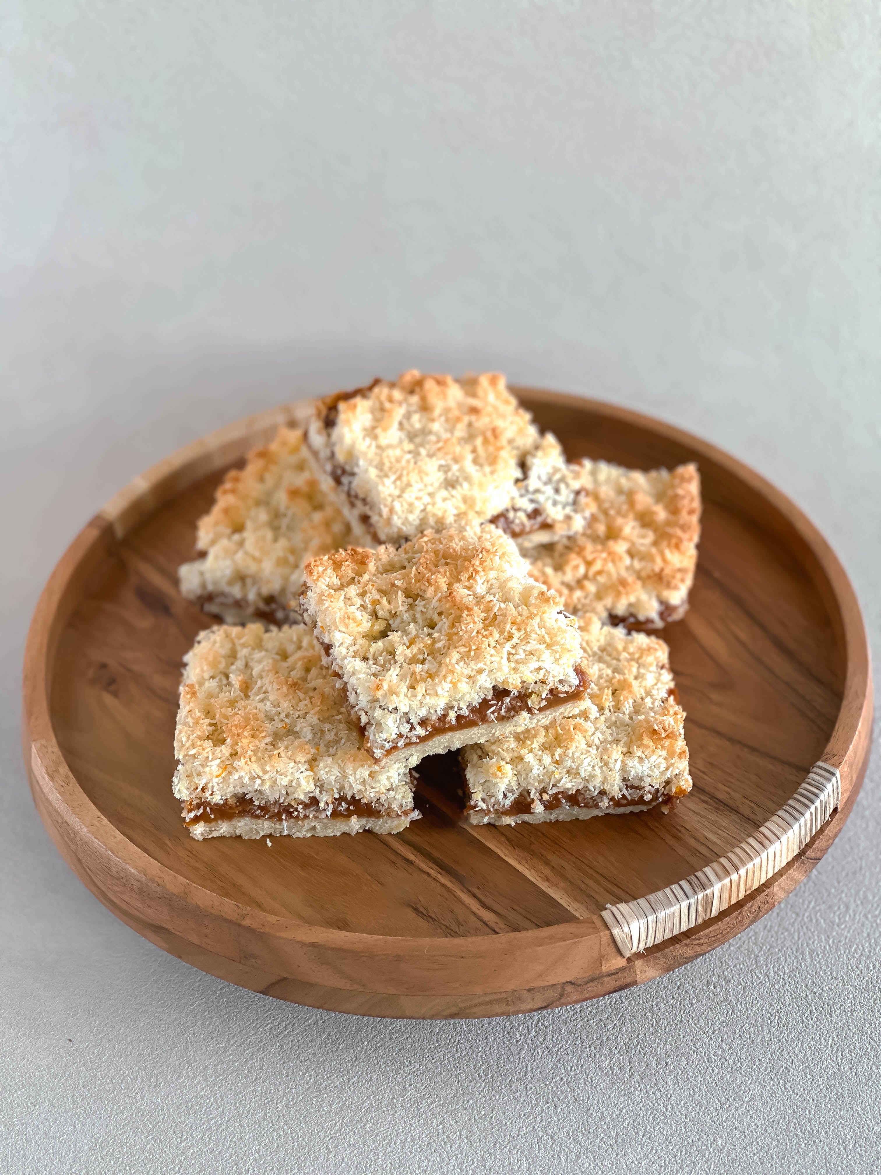 Three coconut dulce de leche dessert bars on a wooden plate with a light gray background.