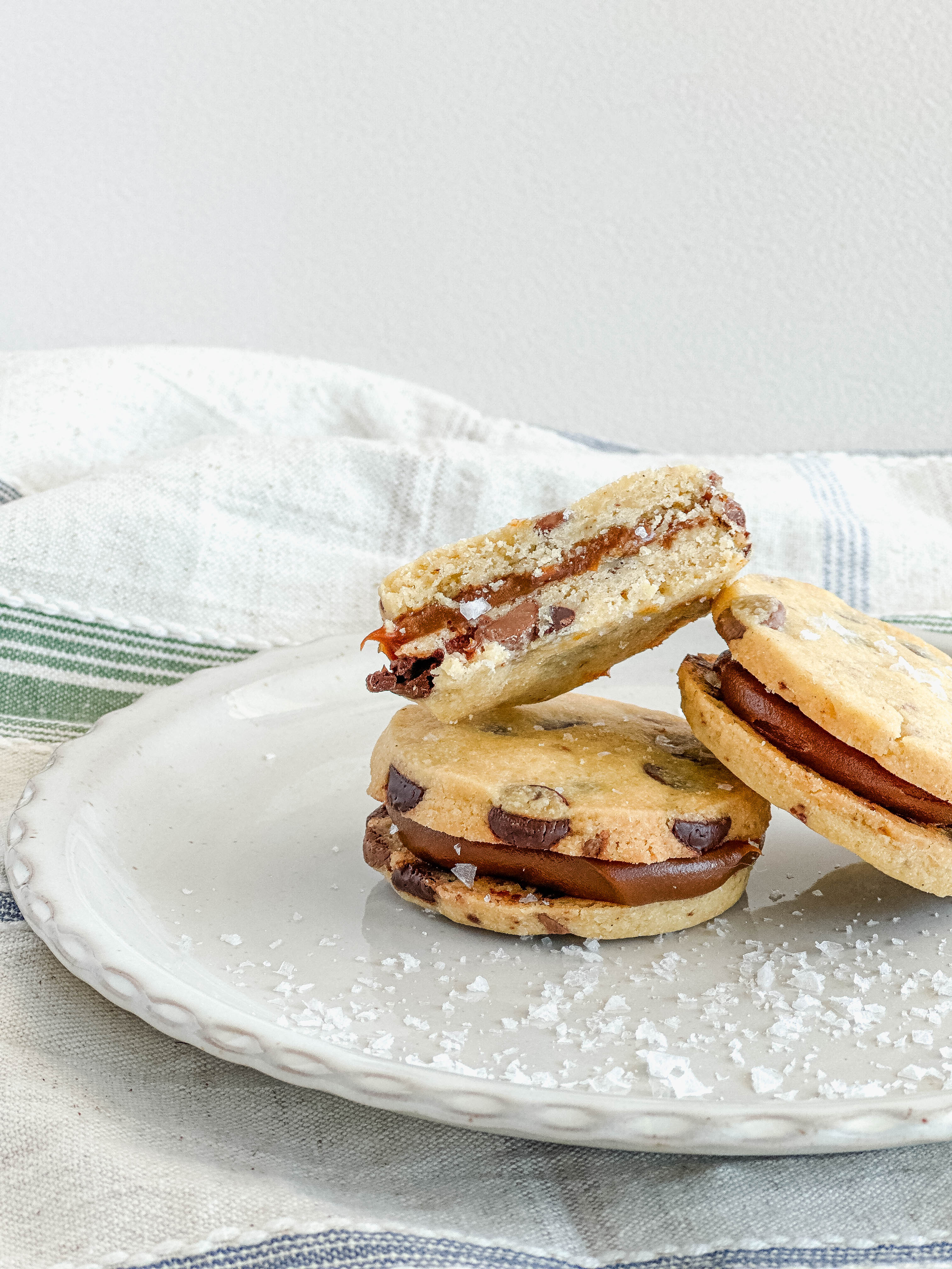 Two alfajores cookie sandwiches with dulce de leche filling on a white plate with a light background.