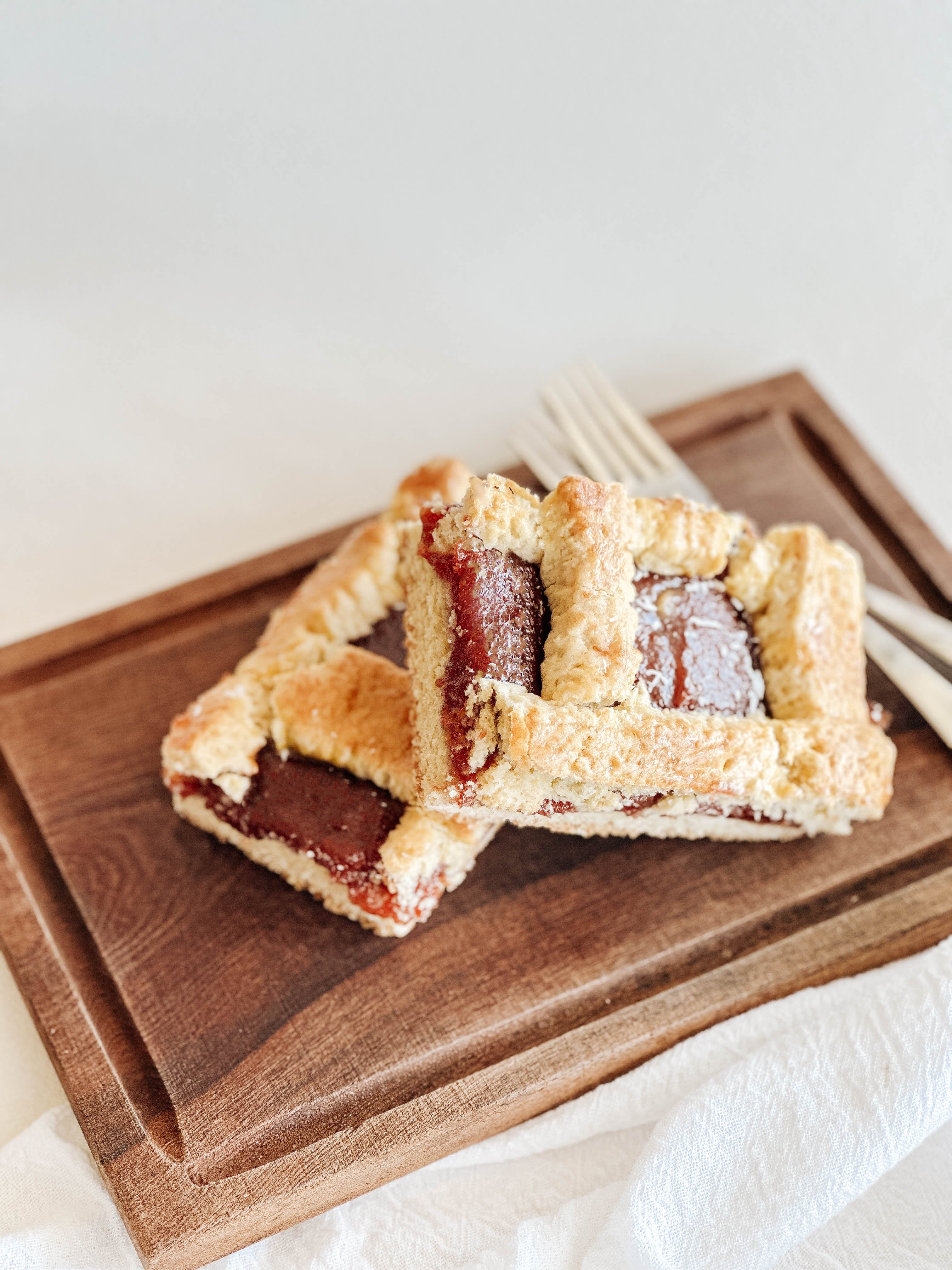 Two slices of guava tart on a wooden cutting board with a white background.