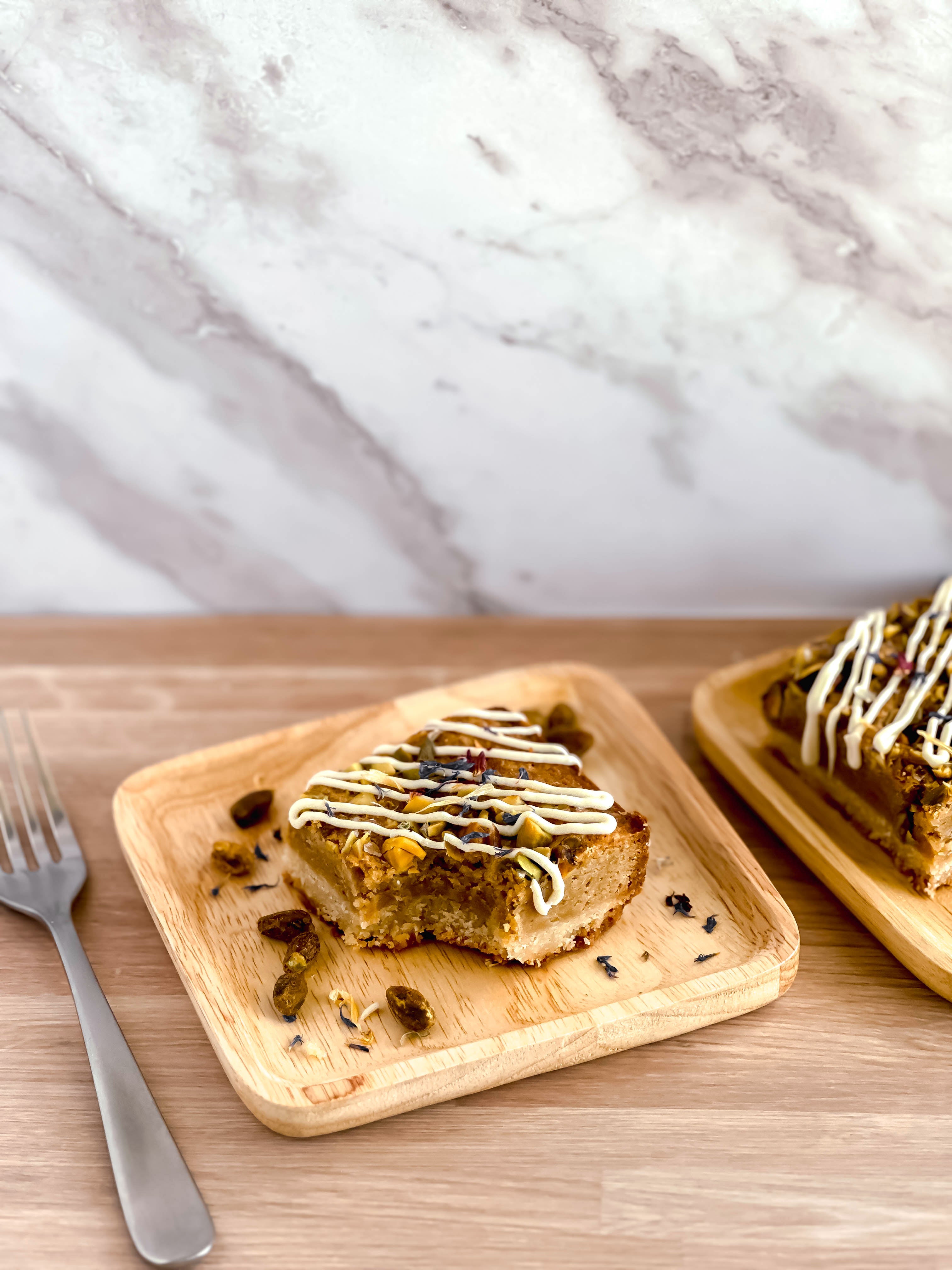 Two slices of honey pistachio bars on wooden plates with a marble background