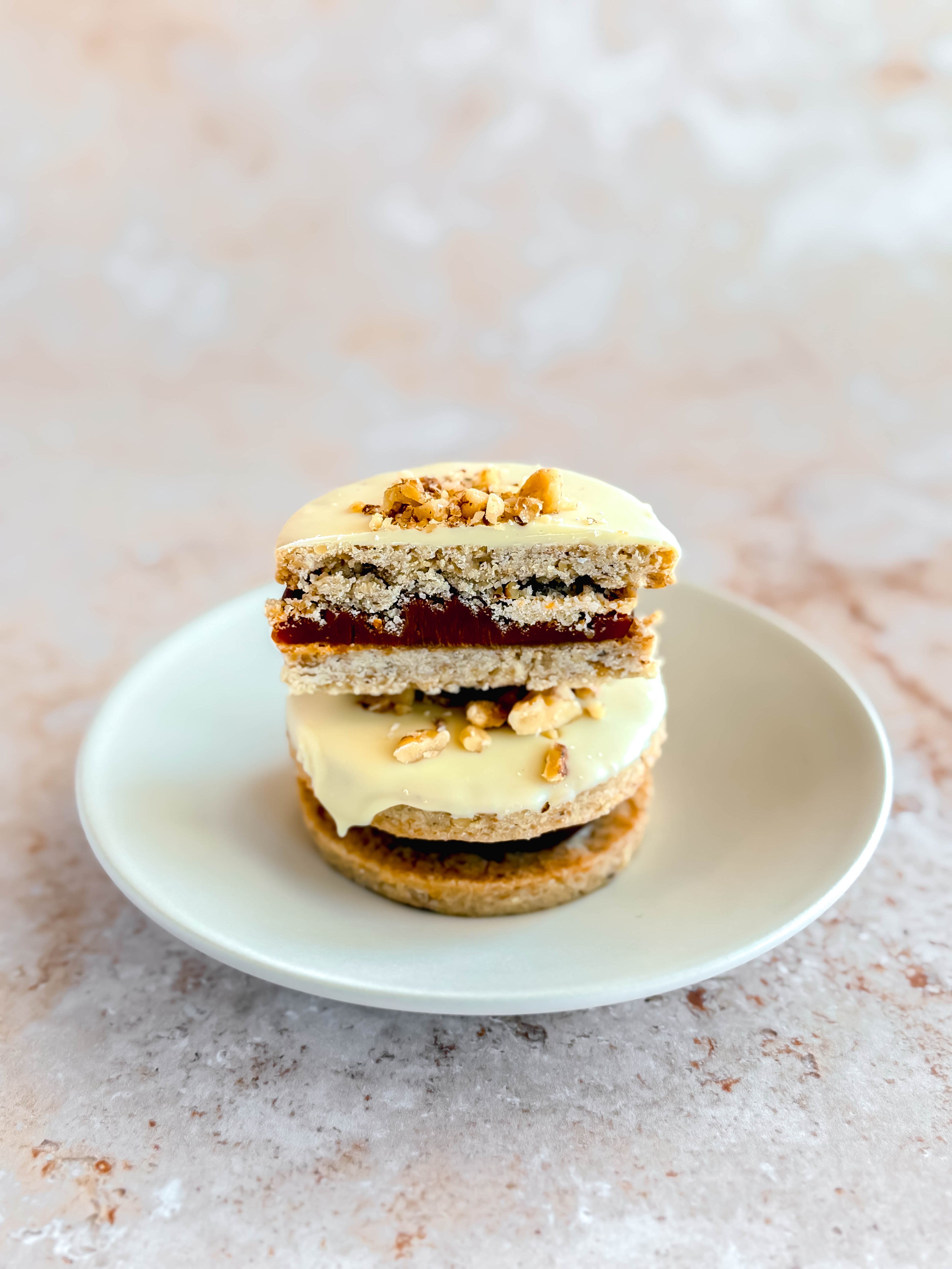 two walnut alfajores on a plate. top alfajor is cut in half to show the filling of dulce de leche