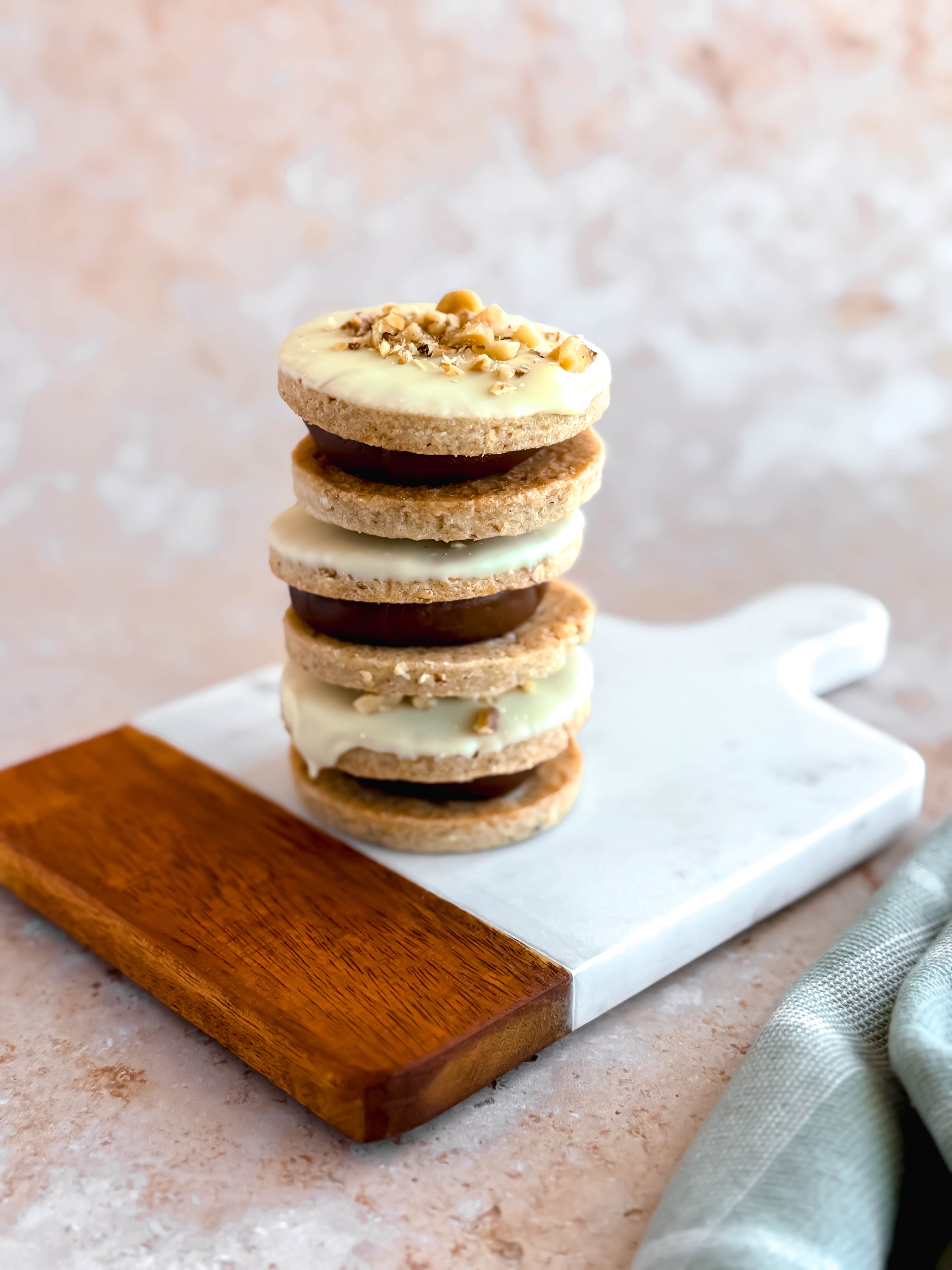 three walnut alfajores on top of each other, filled with dulce de leche and topped with belgian white chocolate
